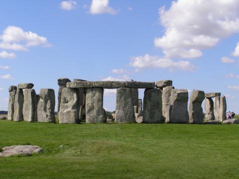 Stonehenge in England, showing a circle of large standing stones topped with horizontal lintels on a grassy plain under a blue sky with scattered clouds