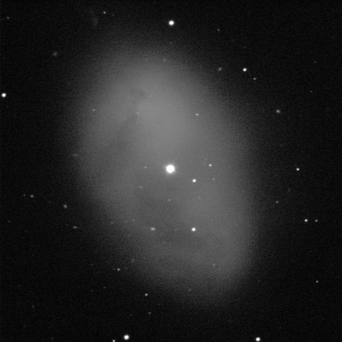 A large, grey, egg-shaped nebula against a black background with some white dots of stars. In the middle of the nebula, a larger, white star shines brightly.