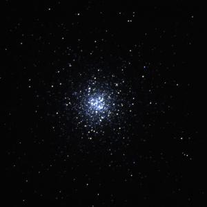 An image of a star cluster against a black background. Small dots of stars are mostly concentrated in the centre, many of them white in colour but some of them having a blue hue to them. Further out from the middle, a few more stars are scattered around, but they are fewer in number and seem more reddish compared to the others.