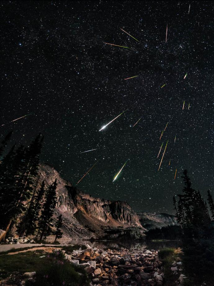 The meteors appear as streaks of light, with varying colors indicating different compositions. The dark, star-filled sky provides a perfect backdrop for this celestial event