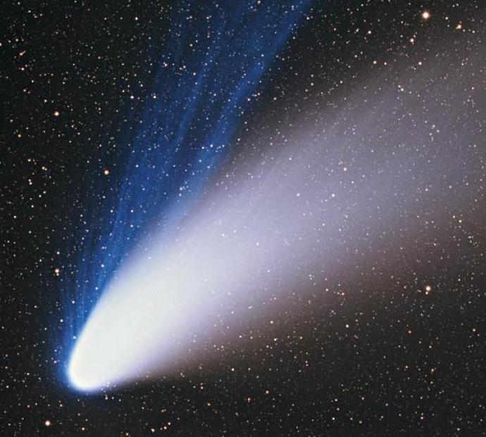 An image of Comet Hale-Bopp, displaying a bright nucleus with a glowing white and blue tail, extending across the star-filled background of space