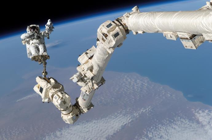 Astronaut performing a spacewalk attached to the Canadarm2 robotic arm with Earth visible in the background